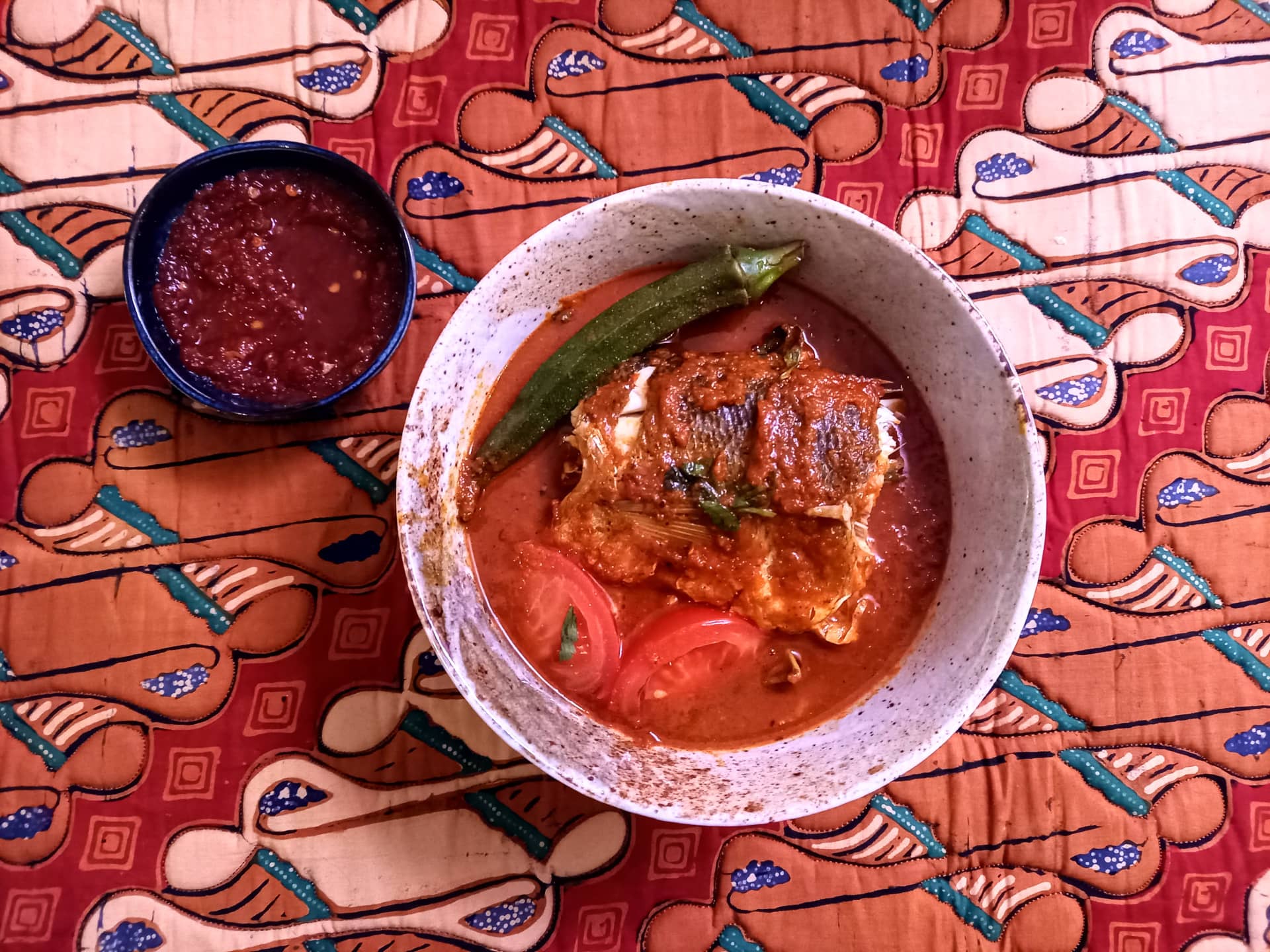 A earthen bowl of asam pedas, next to a small bowl of sambal.