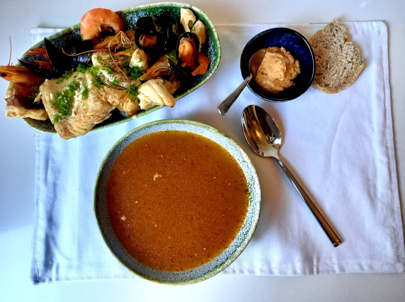 A shallow bowl with bouillabaisse next to a platter containing shellfish and chunks of stewed fish.