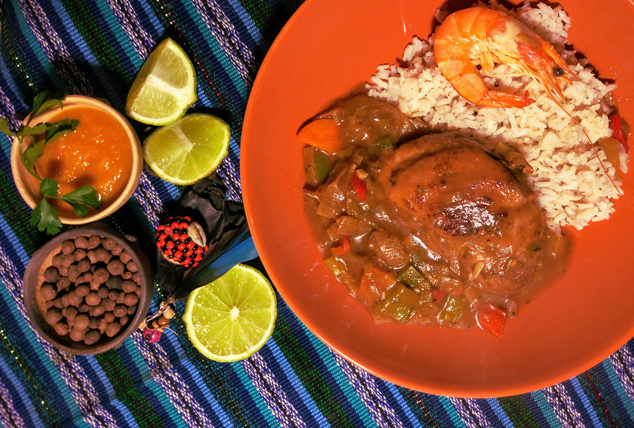 Brown Stew Chicken next to some lemon wedges and spices.