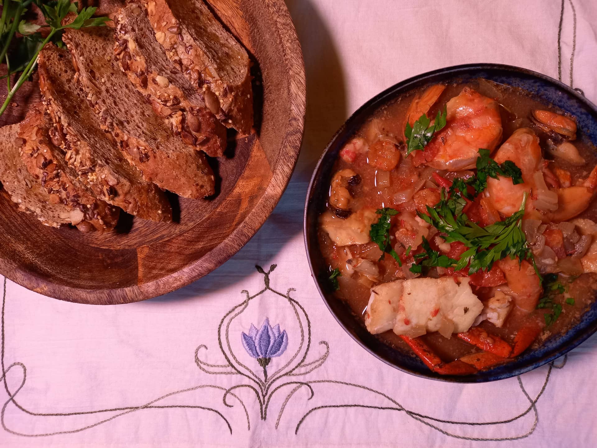 A deep plate with white fish and shellfish sided with toasted bread and olive oil.