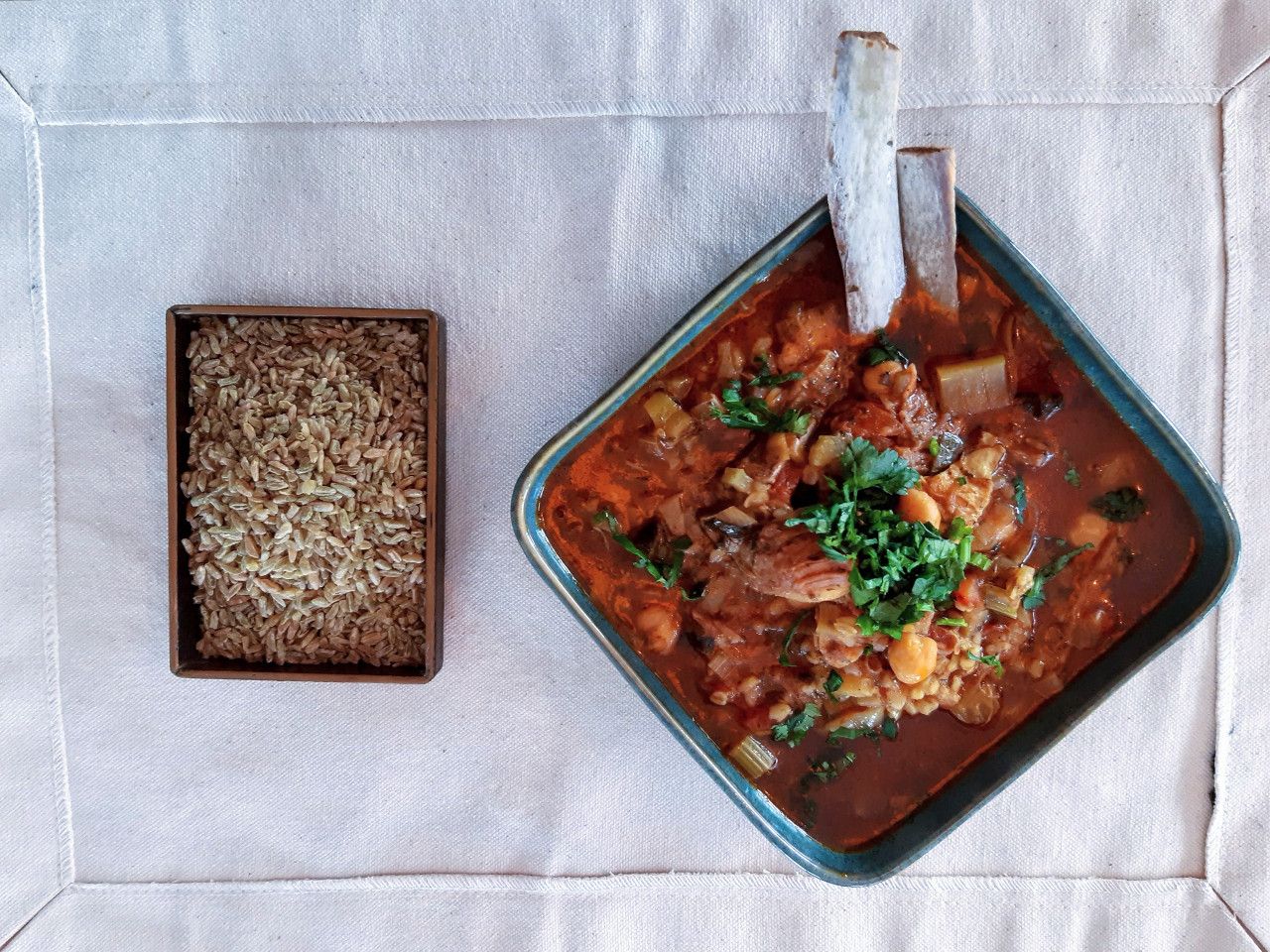 A bowl of Chorba Freekeh Stew next to a rectangular box of freekeh.