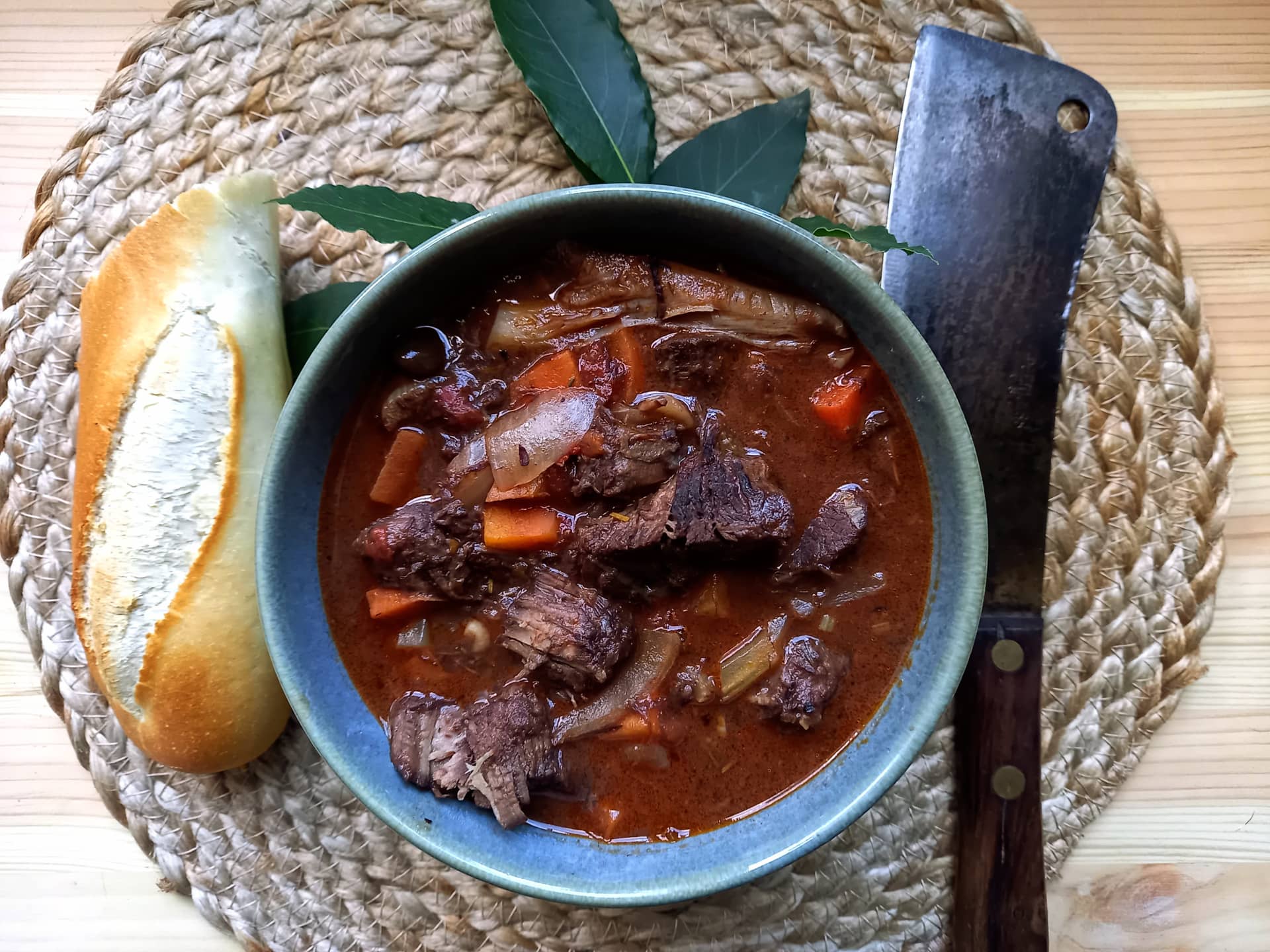 A piece of bread, a cleaver and a bowl of cinghiale in umido.