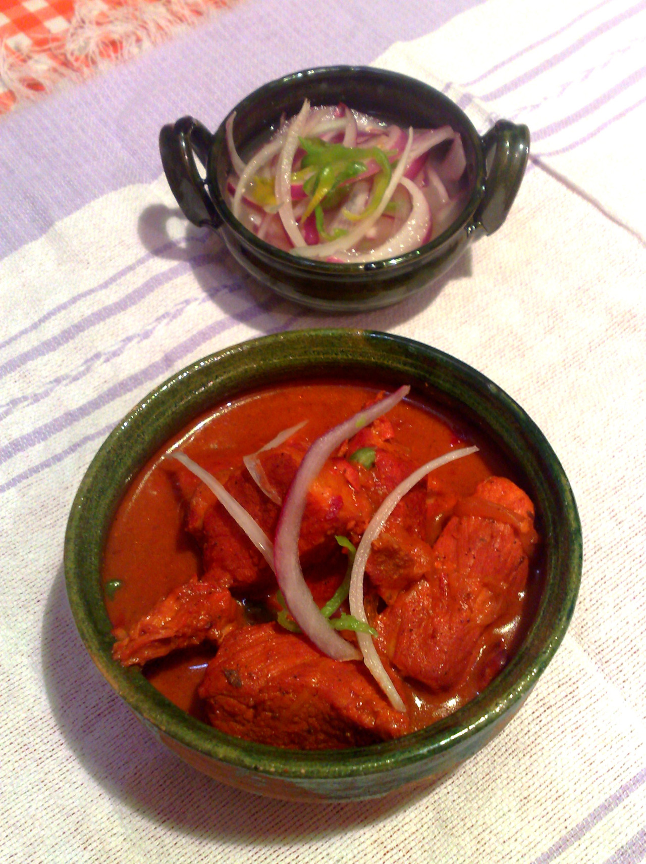 An erthenware bowl with Cochinita Pibil and garnished with red onions.