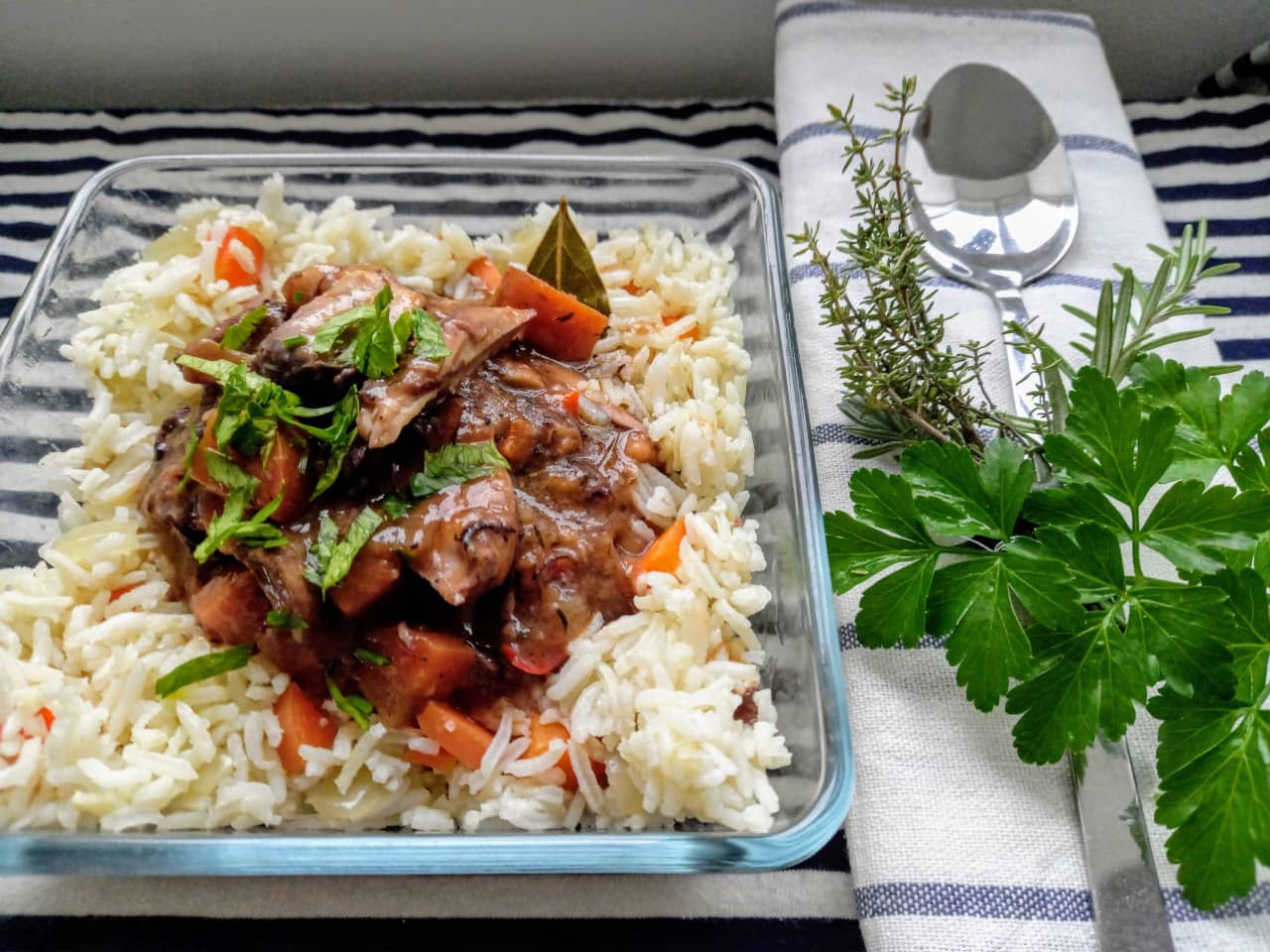 A serving of Coq au Vin garnished with parsley and next to a small bouquet garni.