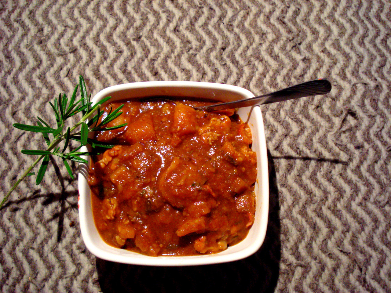 Daube served in a square bowl with a rosemary garnish.