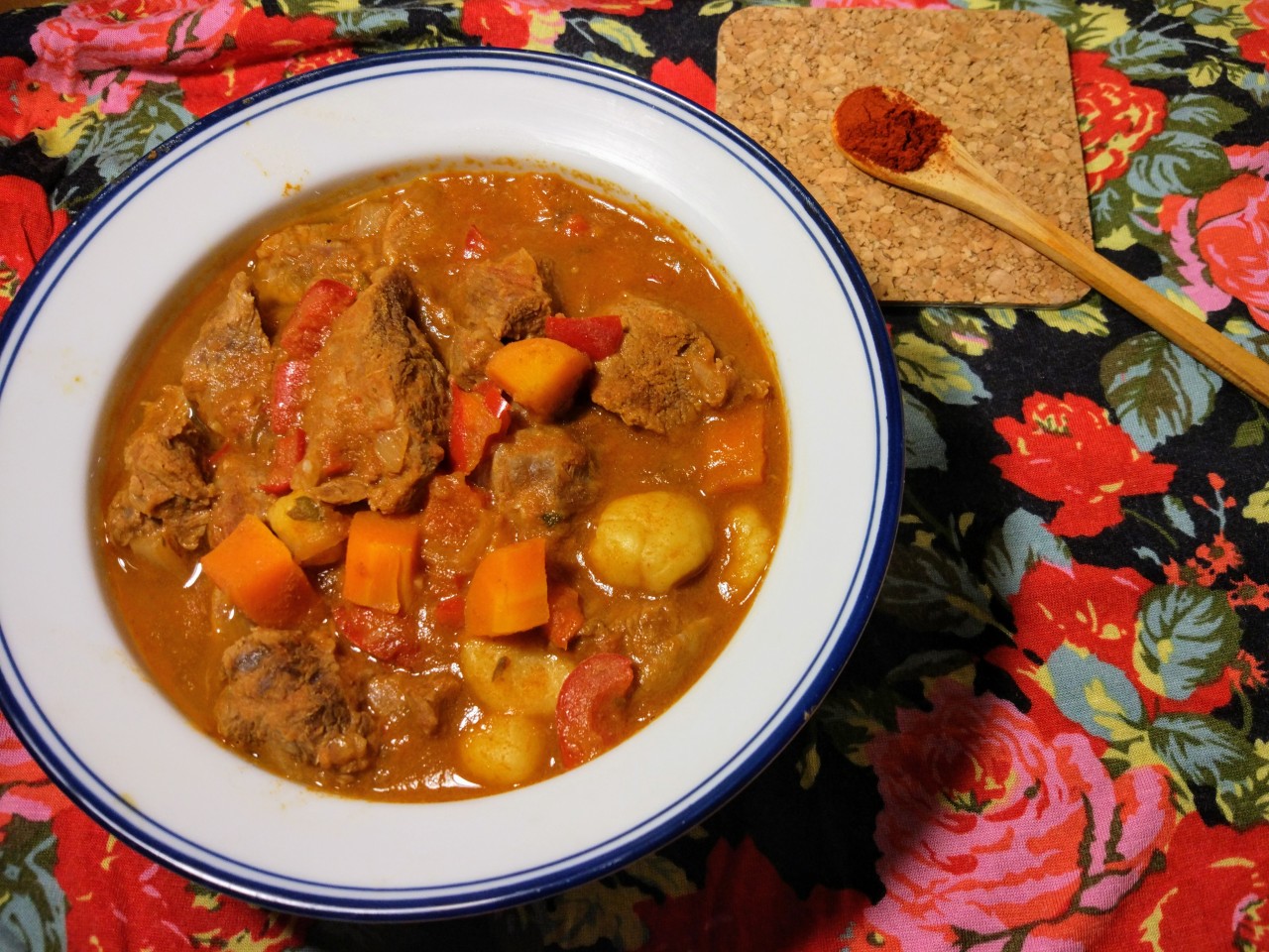 A goulash stew in a bowl with a little wooden spoon with paprika next to it.