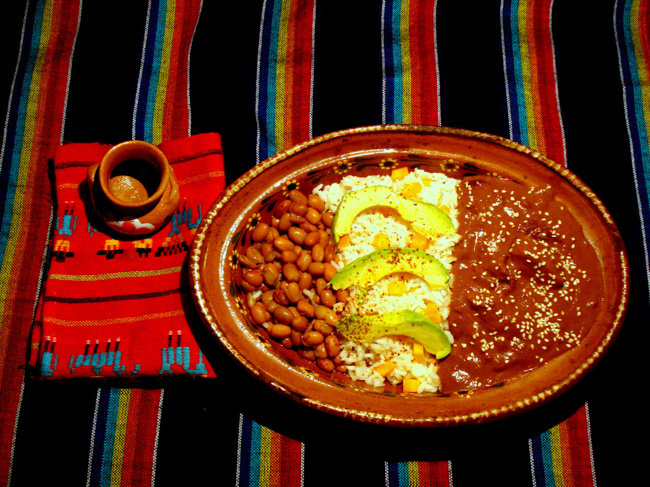 A clay plate with beans, rice and red mole.