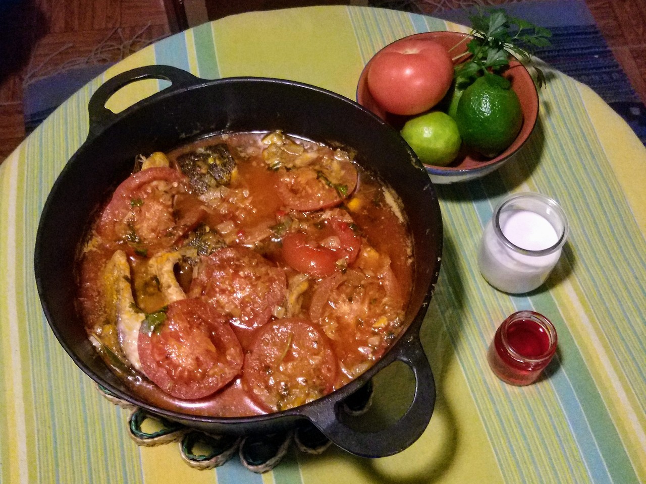 A cast iron pot filled with moqueca next to some coconut milk and palm oil.