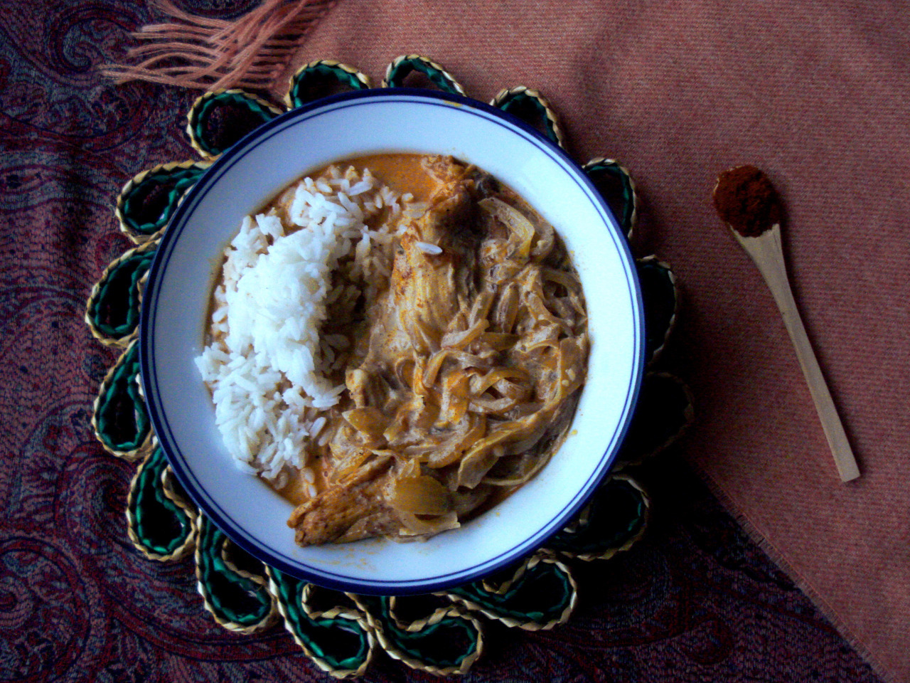 A plate with Paprikáscsirke next to a small wooden spoon with paprika.