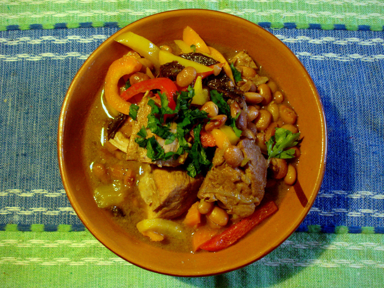 A bowl with beans, pork and vegetables.