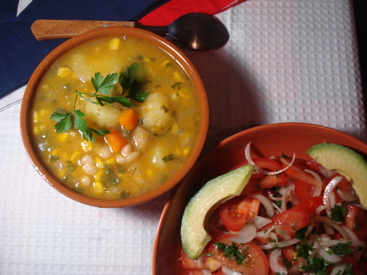 A bowl of porotos granados stew with potatoes next to a traditional Chilean salad.
