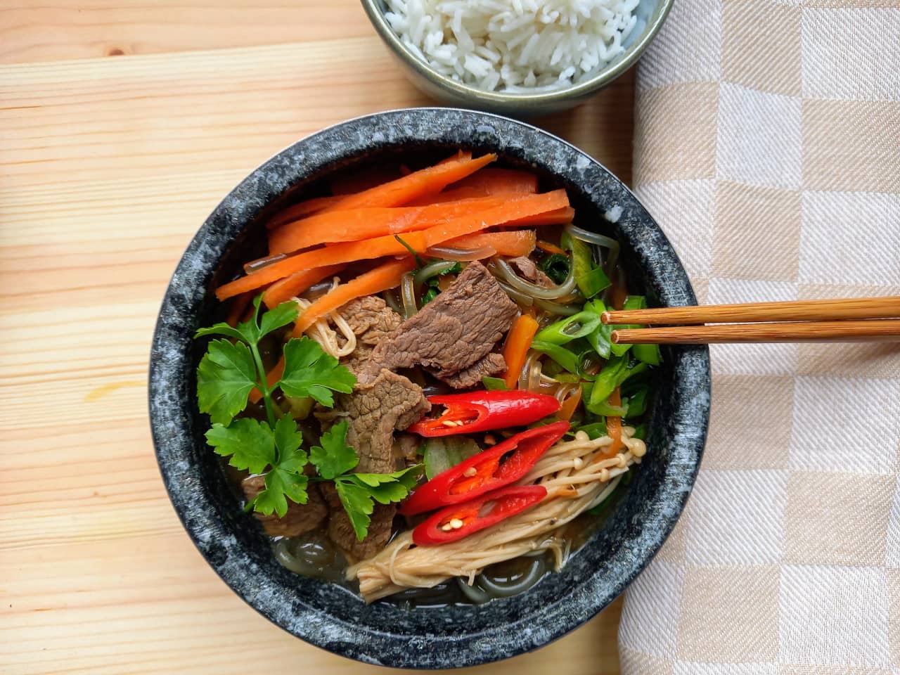 A stew with beef, carrots, enoki mushrooms in a stone bowl.